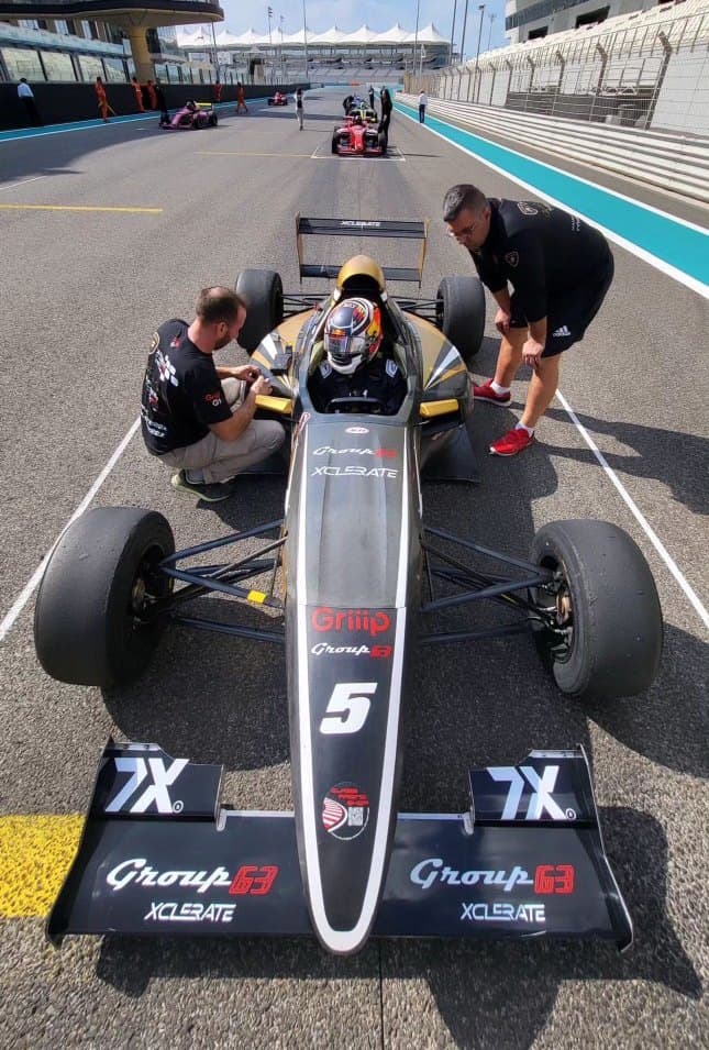 A Formula 4 car on the grid at Yas Marina Circuit with mechanics around it
